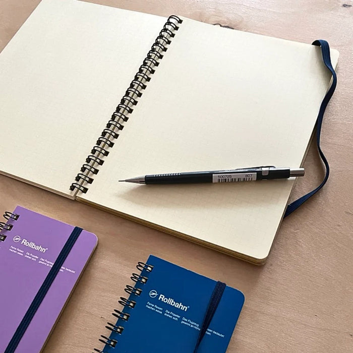 Open Rollbahn notebook on a wooden desk with a mechanical pencil and two smaller notebooks beside it.