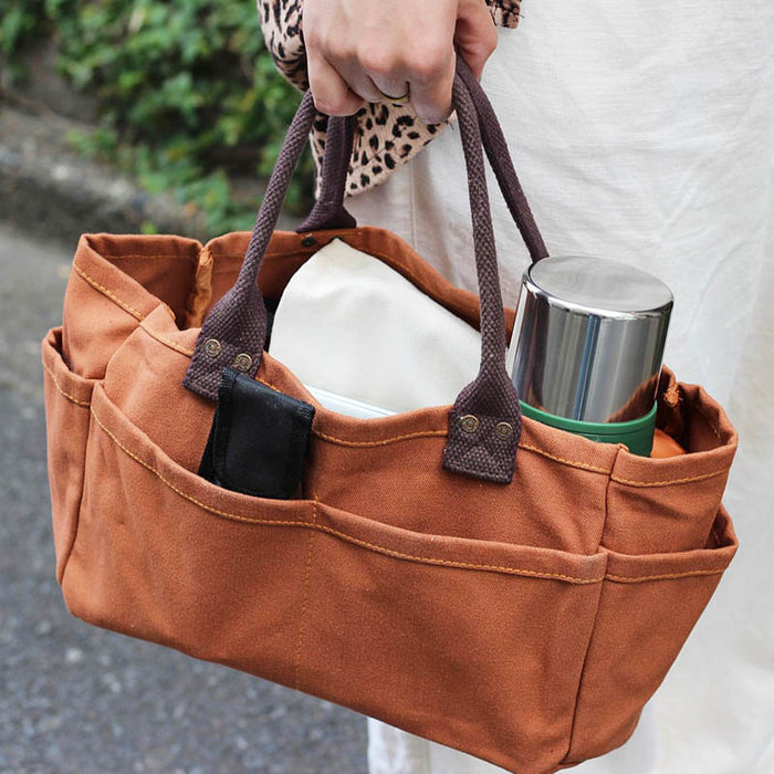 The Journal Shop - A person carrying a brown Dulton Canvas Shoulder Tote Bag filled with a water bottle.