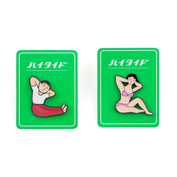 Pair of enamel pins depicting a man and woman in stretching poses, displayed on green backing cards with Japanese text.