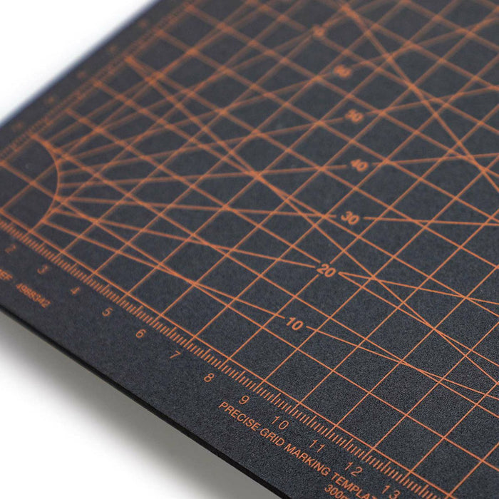 Close-up of a black cutting mat featuring orange precision grid lines and measurement markings.