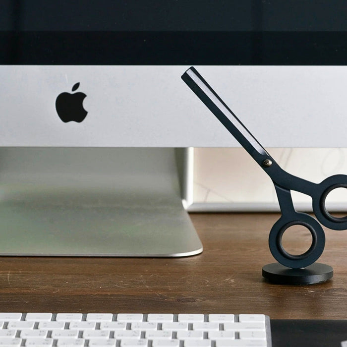HMM Scissors Base aluminium stand in black positioned on desk with scissors for practical use