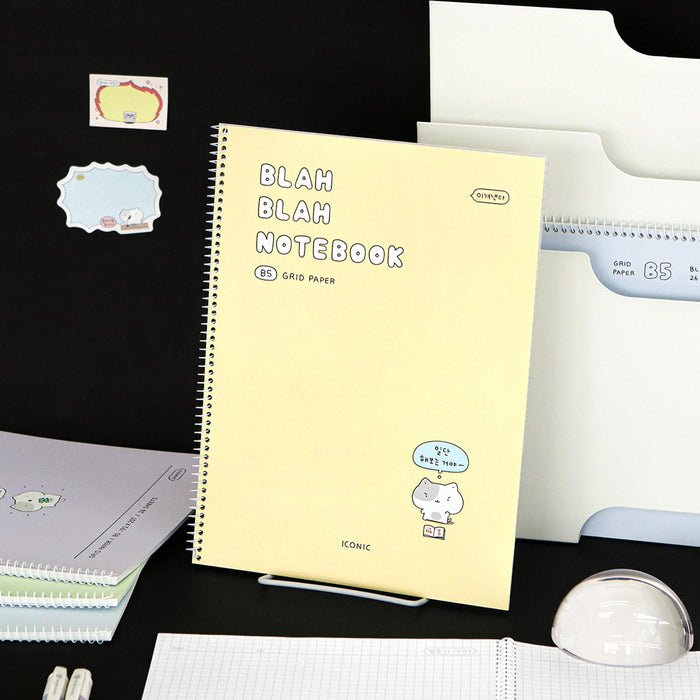 The Journal Shop - Iconic Blah Blah B5 Spiral Grid Notebook cream yellow cover displayed with black background and decorative items.