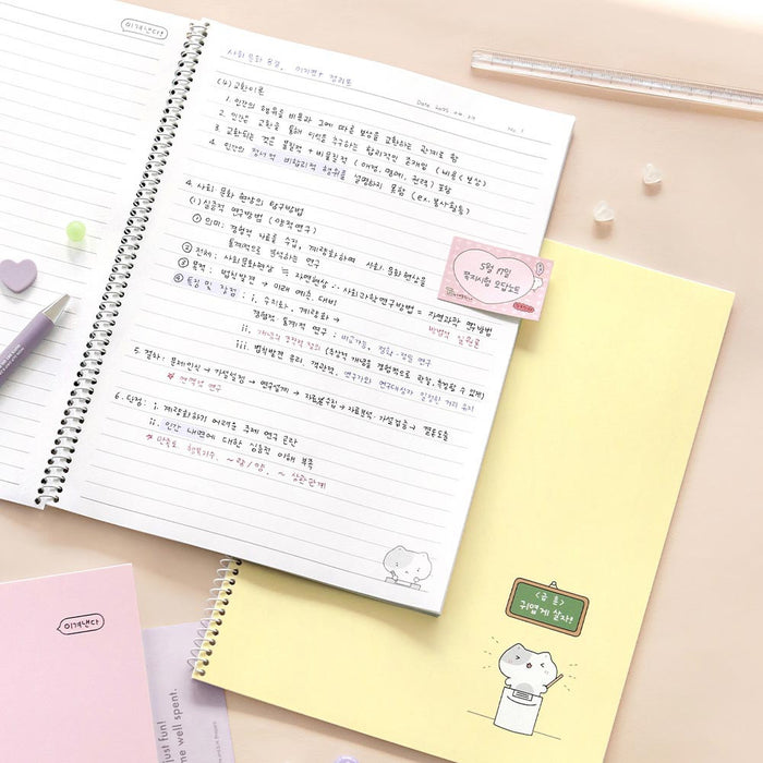 The Journal Shop - Iconic Blah Blah B5 Spiral Lined Notebook open on desk with writing and pastel yellow notebook beneath.