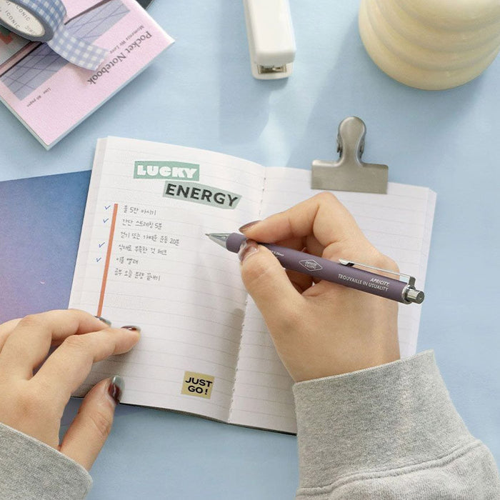 Hand writing in the Iconic Daily Life Pocket Notebook v.3 lined edition at a desk.