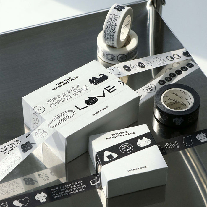 The Journal Shop - Close-up of Iconic Doodle Masking Tape in black-and-white designs, displayed on a reflective surface with rolls and packaging boxes.