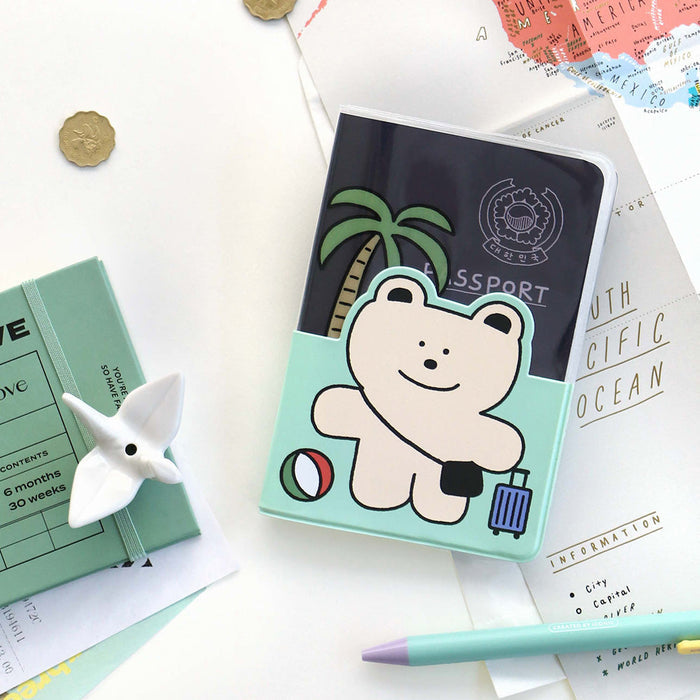 The Journal Shop - Iconic Doodle Passport Case with cheerful character design placed beside travel accessories on a light background.