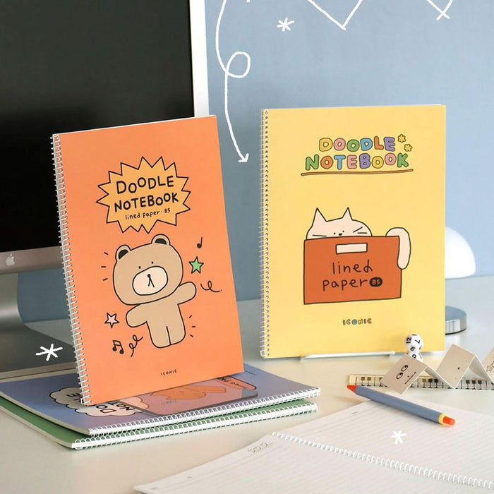 Iconic Doodle B5 Spiral Lined Notebooks in orange and yellow covers displayed on desk beside stationery.