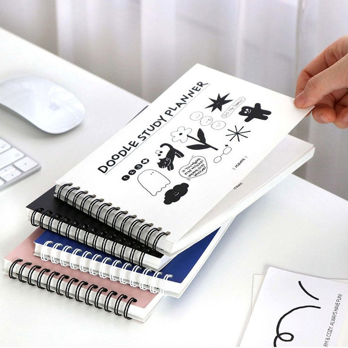 The Journal Shop - Hand flipping through a stack of spiral-bound Doodle Study Planners featuring playful doodle-style illustrations.