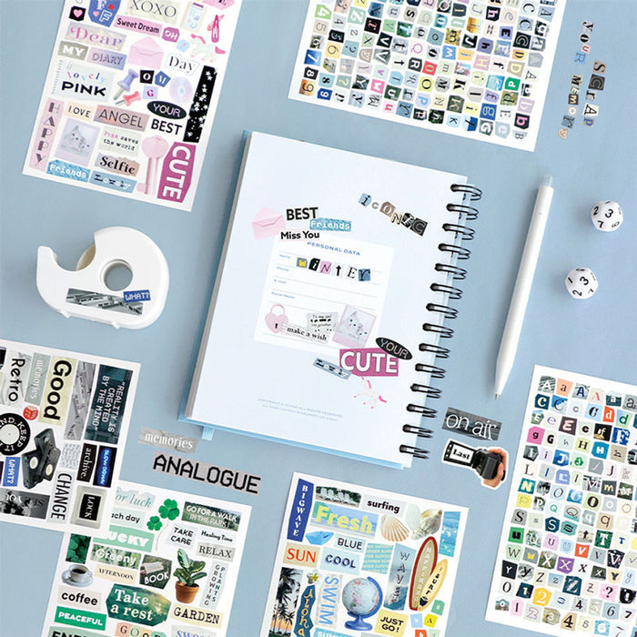 The Journal Shop - Collection of Iconic Magazine Collage Sticker sheets and a spiral notebook arranged neatly on a blue surface.