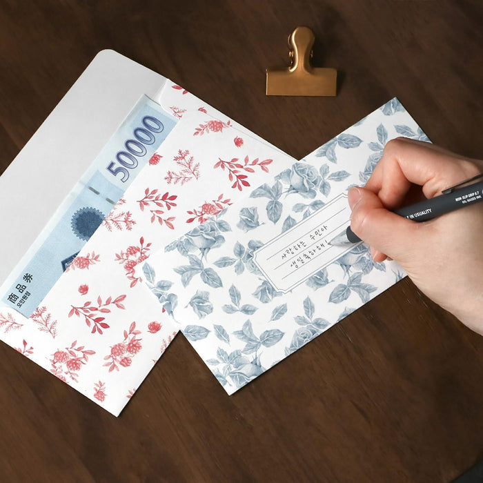 The Journal Shop - Person writing on a floral Iconic Pattern Envelope placed on a dark wooden surface.