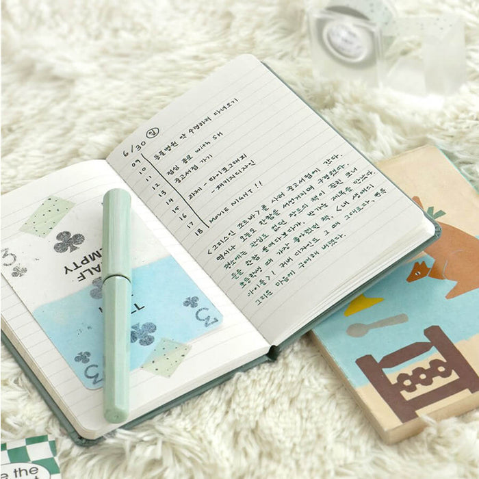 The Journal Shop - Iconic Solitude Handy Notebook open with handwritten notes beside travel photos and small stationery items.