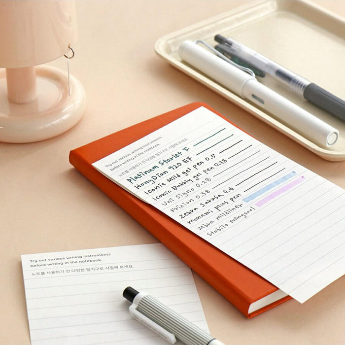 The Journal Shop - Iconic Solitude Handy Notebook orange cover open on tidy desk with pen and small lamp beside it.