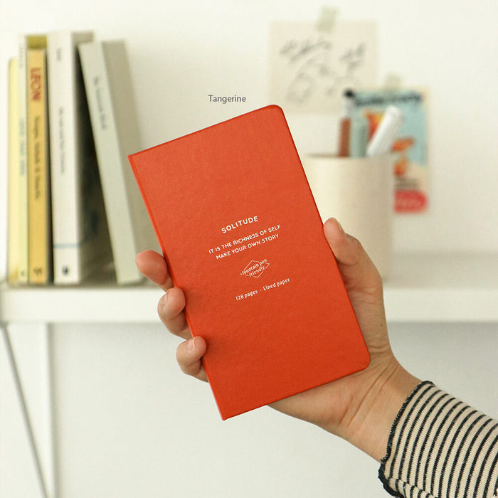 The Journal Shop - Iconic Solitude Handy Notebook orange cover held in hand showing compact B7 size and elegant design.