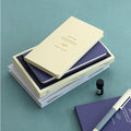 The Journal Shop - Iconic Solitude Handy Notebooks in cream covers lay flat on the table with books and pen.