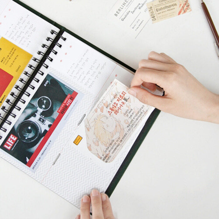 Person using the Iconic Ticket Scrapbook Album to arrange postcards and keepsakes on a page.