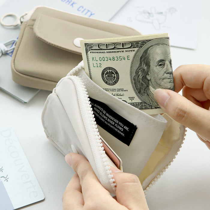 The Journal Shop - Close-up of beige Iconic Voyager Card Wallet with a hand placing cash into the zip compartment.