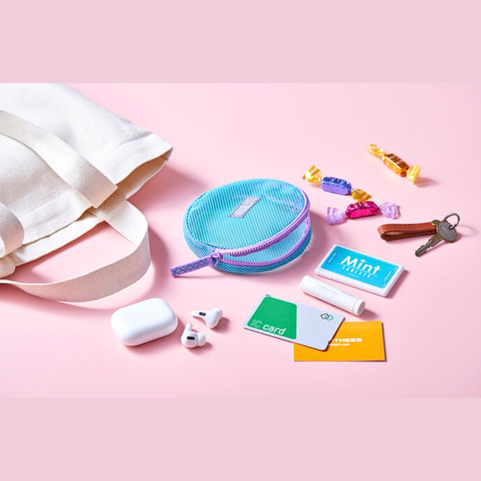 Flat lay of Flatty Sheer transparent pouch with small accessories on a pink background.