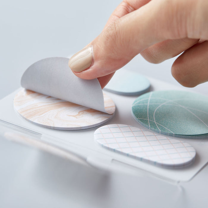 Hand pressing a HITOTOKI Coffret cosmetic sticky note onto a smooth surface.