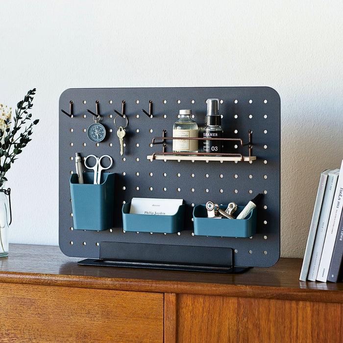 Black PEGGY pegboard stand displayed on a wooden surface in a home office setting.
