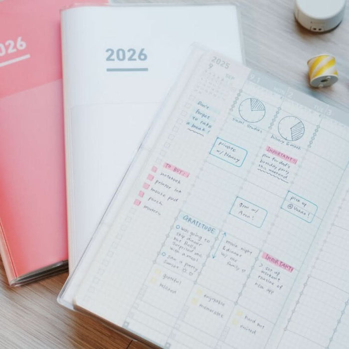 Lifestyle view of Kokuyo Jibun Techo First Kit 2026 open with sample writing on a desk with accessories.