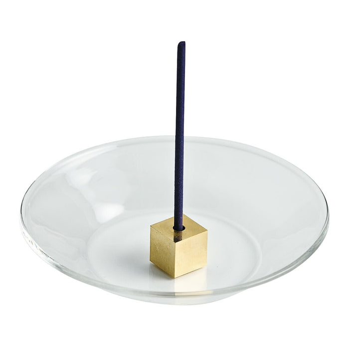 Brass cube incense holder centred on a round glass plate holding a single upright incense stick.