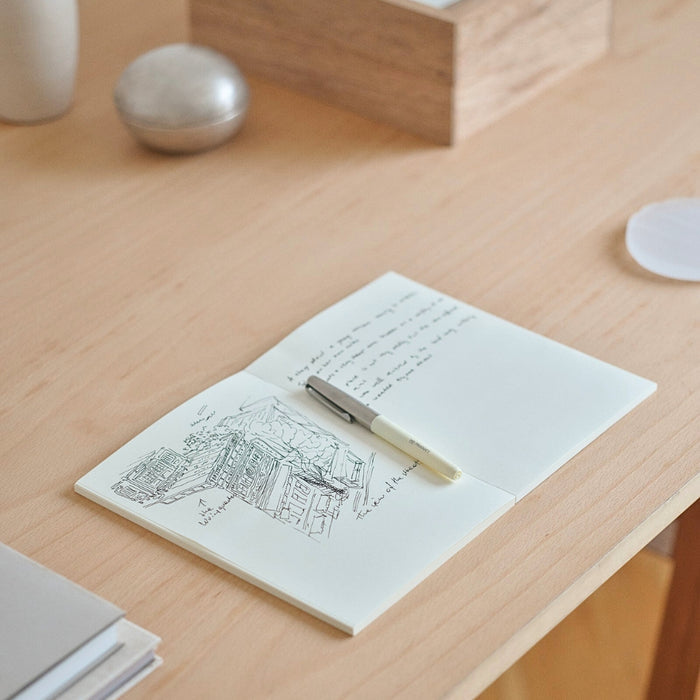 Midori MD Notebook A5 Grid placed on wooden desk with stationery and writing tools.