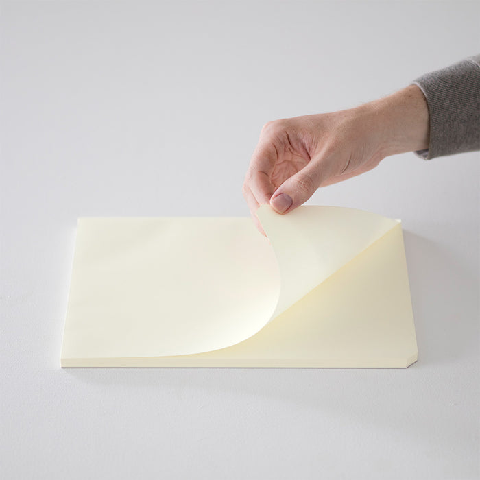 Hand turning a page of the Midori MD Paper Pad, highlighting its double-edge binding and unruled surface.