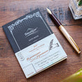 Tomoe River A6 softcover squared notebook on wooden desk with fountain pen.