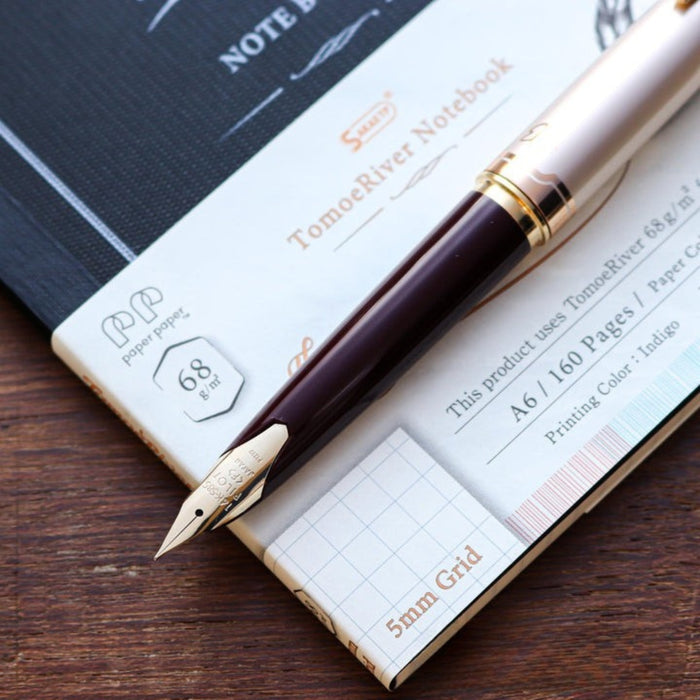 Angled view of Tomoe River A6 squared notebook with gold-trimmed fountain pen.