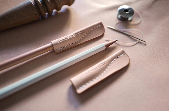 Flat lay of Tools to Live By leather pencil caps on wooden surface.