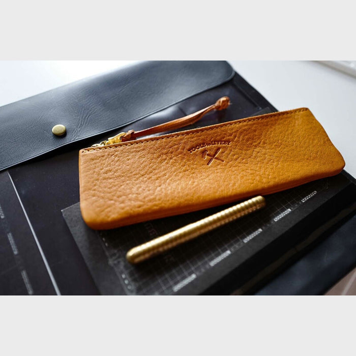 Tan (S) - Tools To Live By tan leather pen case resting on a desk alongside notebooks and stationery.