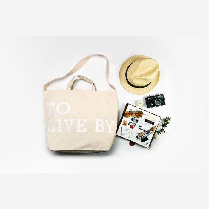 Beige Tools To Live By tote bag laid flat with everyday stationery items.
