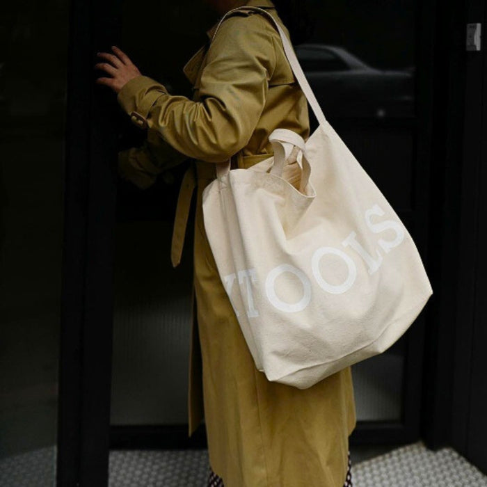 Person carrying beige Tools To Live By tote bag over the shoulder.