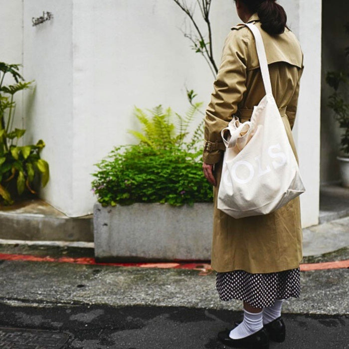 Beige Tools To Live By tote bag worn outdoors as a casual everyday bag.