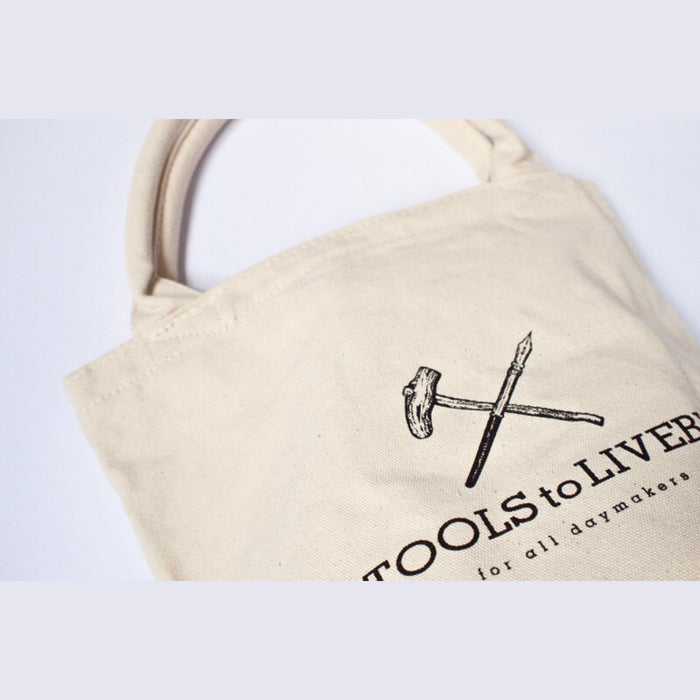 Close-up of Tools To Live By logo printed on a cream canvas tote bag.