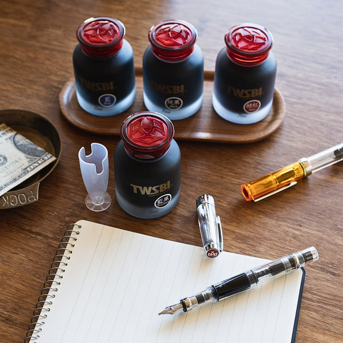 TWSBI fountain pen ink 70ml bottles arranged on wooden desk with pen and notebook.